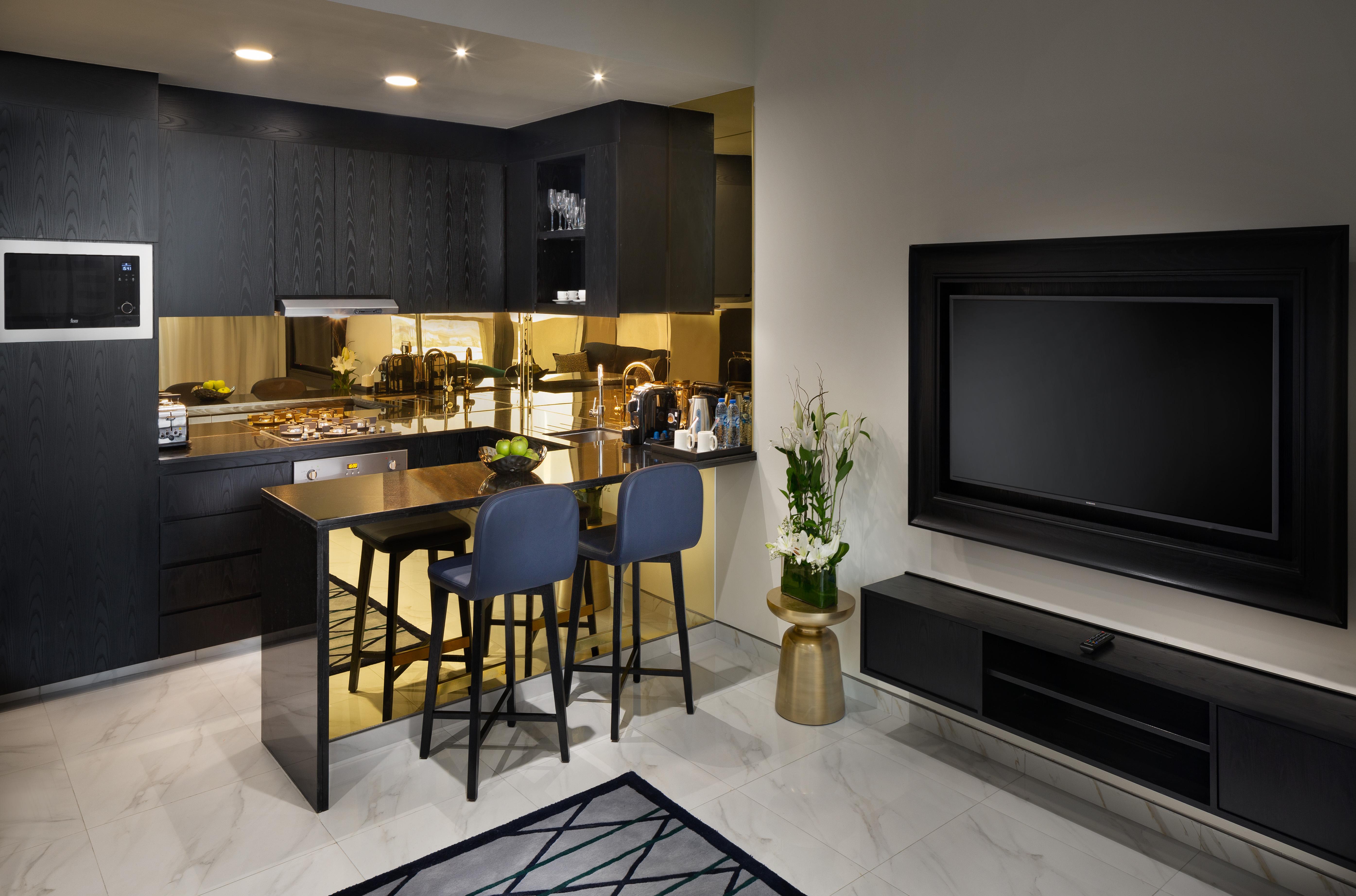 Aparthotel Millennium Atria Business Bay Dubái Exterior foto The photo depicts a modern kitchen and living area. The kitchen features dark cabinetry with a clean design, showcasing various appliances, including a stovetop and possibly an oven. There is a kitchen island with two stools, suggesting a space for c