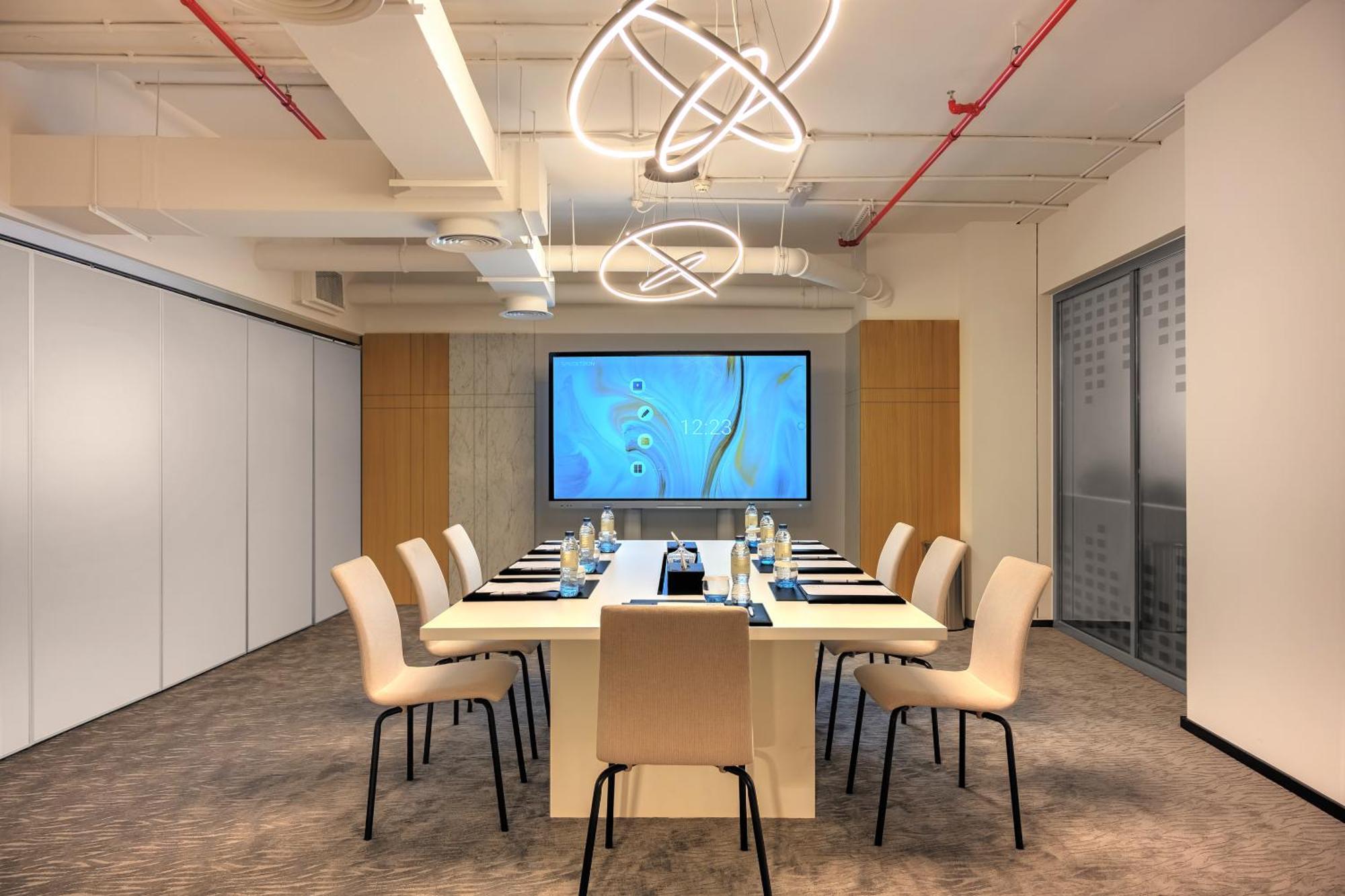 Aparthotel Millennium Atria Business Bay Dubái Exterior foto The photo shows a modern conference room designed for meetings. It features a long white table surrounded by beige chairs. At the end of the table, there is a large screen displaying a blue abstract design. The room is well-lit with contemporary ligh