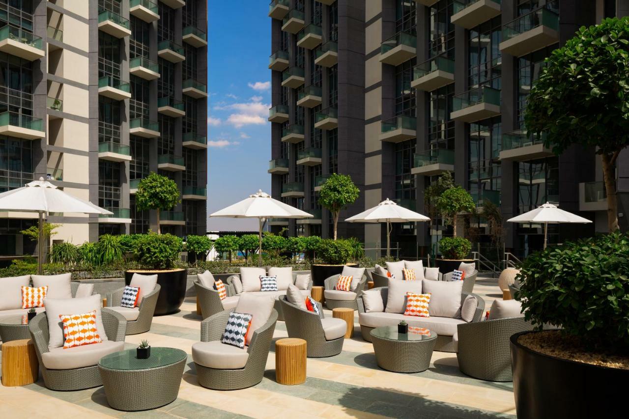 Aparthotel Millennium Atria Business Bay Dubái Exterior foto The photo shows a modern outdoor lounge area, featuring several comfortable seating arrangements made of soft, stylish lounge chairs and round tables. The seating is adorned with colorful pillows, adding a pop of color to the neutral tones of the fur