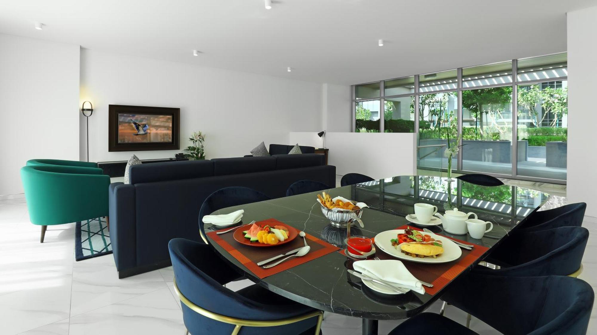 Aparthotel Millennium Atria Business Bay Dubái Exterior foto The photo depicts a modern living space with a dining area and a seating area. In the foreground, there is a round dining table set with plates of food, including eggs, toast, and a small bowl of fruit, accompanied by cups and napkins. The table is c
